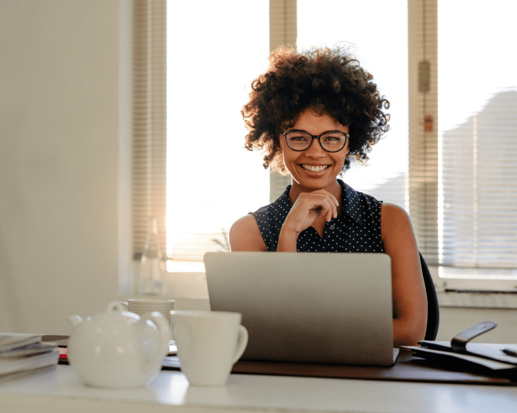 Coloured woman smiling while sitting in front of her laptop at her desk
