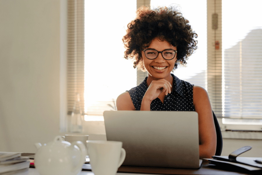 Coloured woman smiling while sitting in front of her laptop at her desk